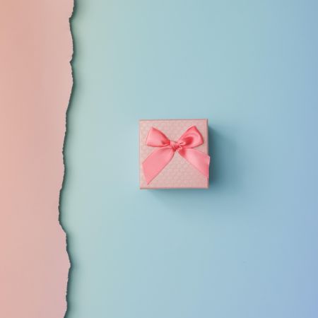 Close up shot of small gift wrapped with pink ribbon on pink blue background