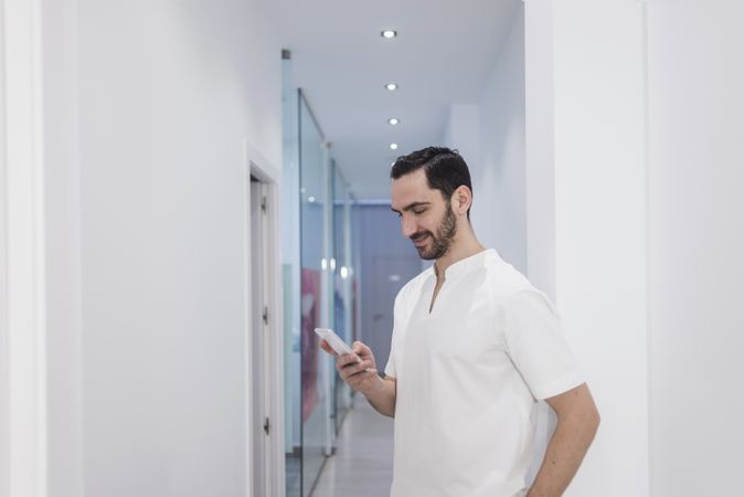 Smiling bearded male doctor, medical professional using a smartphone mobile phone at hospital