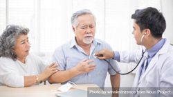 Doctor with stethoscope on worried Asian male patient’s chest bDGop4