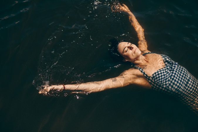 Woman in swimsuit relaxing in water with closed eyes