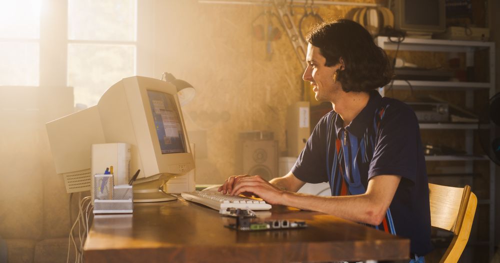 White Male Software Engineer Programming On Old Desktop Computer In Retro Garage With Random Appliances.