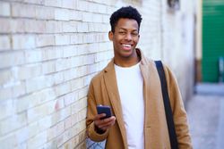 Smiling Cuban male leaning against wall holding his phone