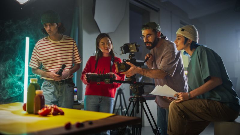 Diverse Young Film Crew Engaged In A Creative Video Production Session On A Vibrant Set, Surrounded By Modern Equipment And Colorful Props, Focusing On Capturing Engaging Content For A Dynamic Project