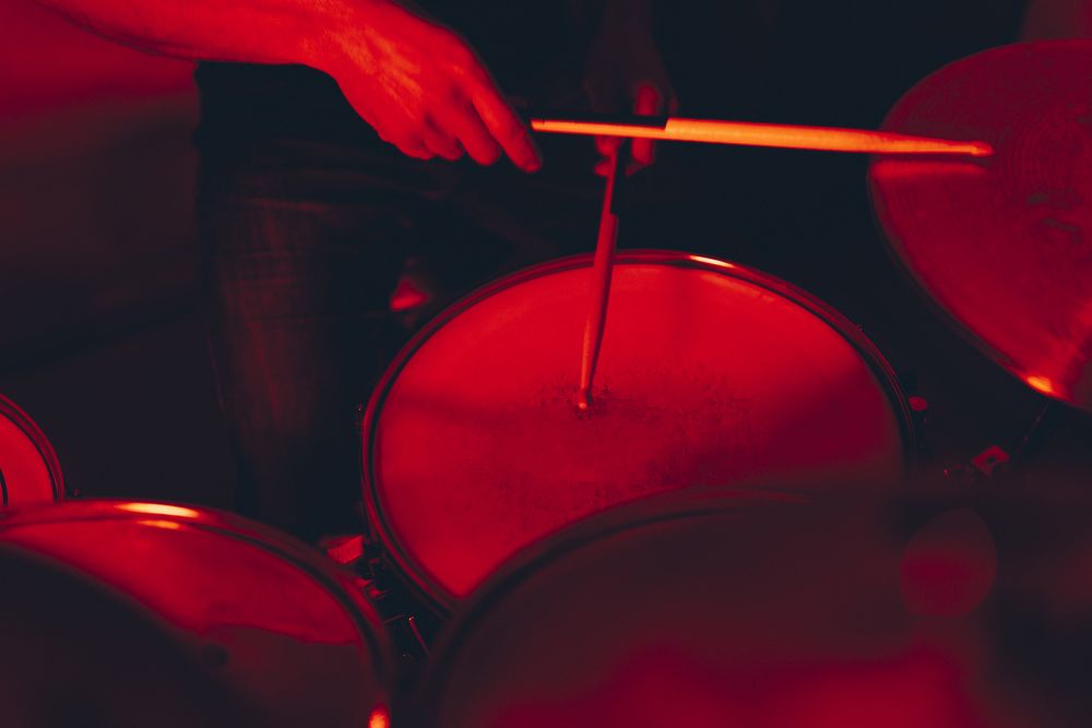 Anonymous man with drumsticks playing on drums in redness