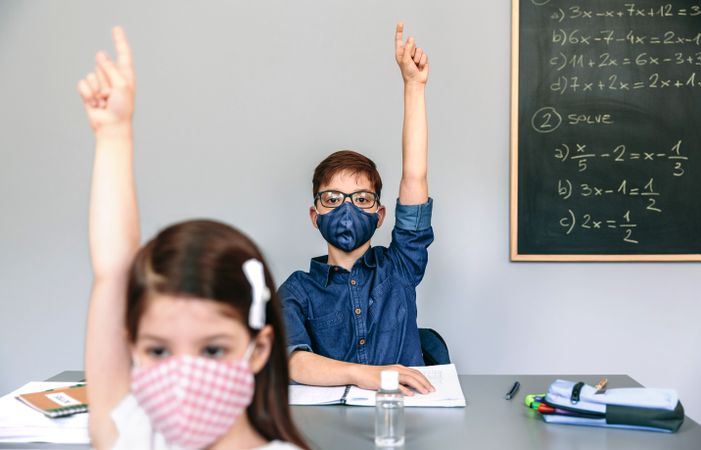 Students with masks raising hands at school