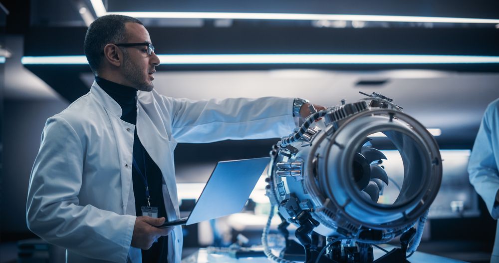 Male Project Leader Holding a Laptop Computer and Explaining the Innovative Technology in Scientific Technology Lab