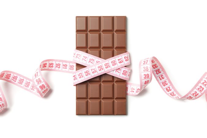Measuring tape and chocolate bar on blank background