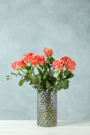 Vase with orange roses on table against light background