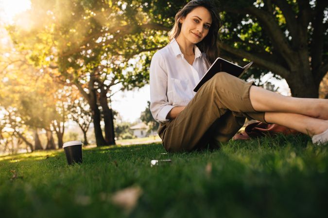 Woman sitting on grass with a coffee reading book