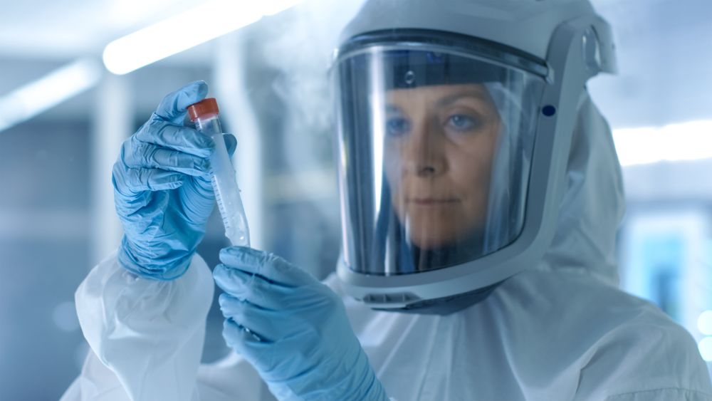 Medical Virology Research Scientist Works in a Hazmat Suit with Mask, She Inspects Test Tube with Isolated Virus String from Refrigerator Box.