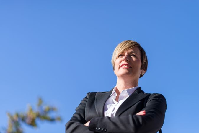 Proud businesswoman standing with arms crossed against blue sky
