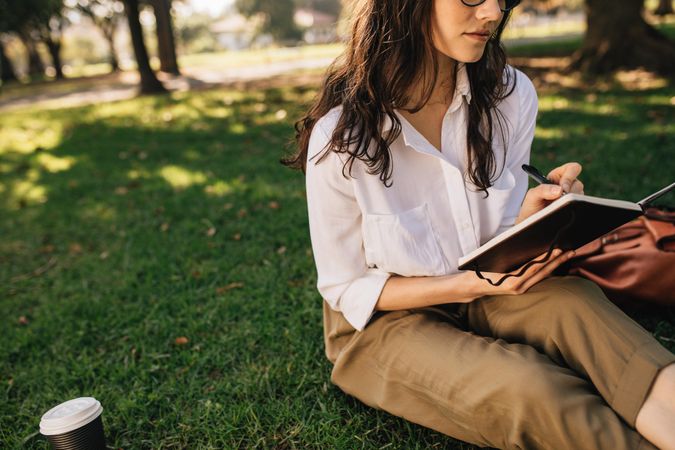Woman sitting on grass at park with book making notes