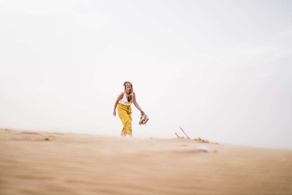 Happy woman holding shoes in desert