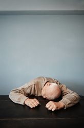 Exhausted man feeling headache and negative emotions while sitting at the table