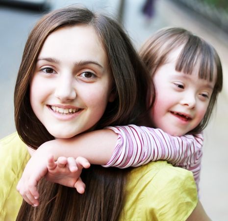 Portrait of a young girl with Down syndrome on her sister’s back in the park