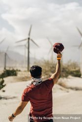 Man holding hat up and standing beside wind turbine field 5qQYJ5