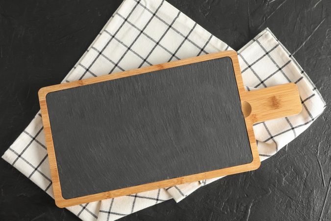 Cutting board with kitchen towel on dark background, top view