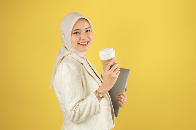 Asian Business Woman in Cream Suit and Hijab Holding a Laptop and Hot Coffee Cup