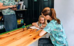 Mother helping her daughter with homework while father works with tablet in their own coffee shop
