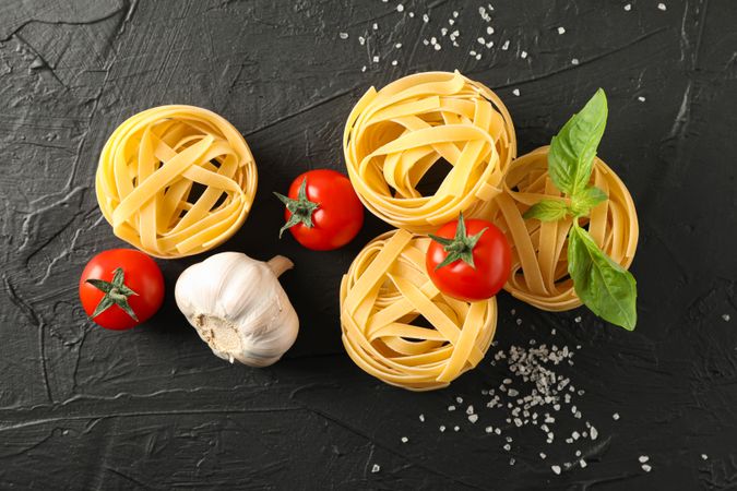 Composition with pasta, tomatoes, salt and garlic on dark background, space for text