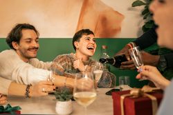 Joyful woman laughing while friends pour champagne at a Christmas celebration.