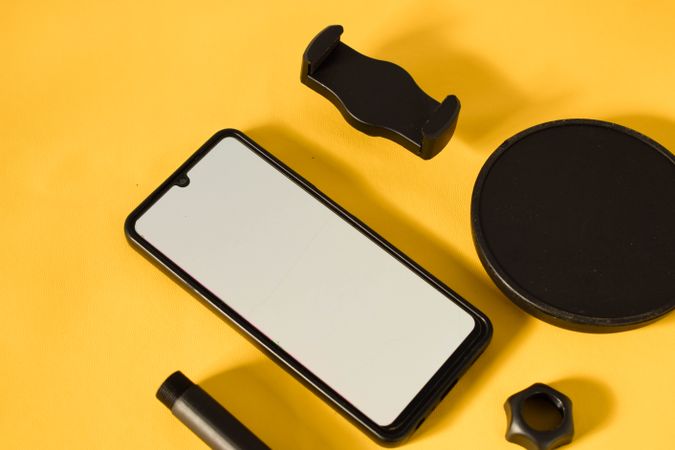 Phone with mockup screen and accessories scattered on yellow table with shadow and copy space