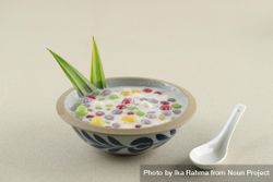Thai dessert of colorful rice balls in sweet coconut milk on beige table with spoon 0JmVNb