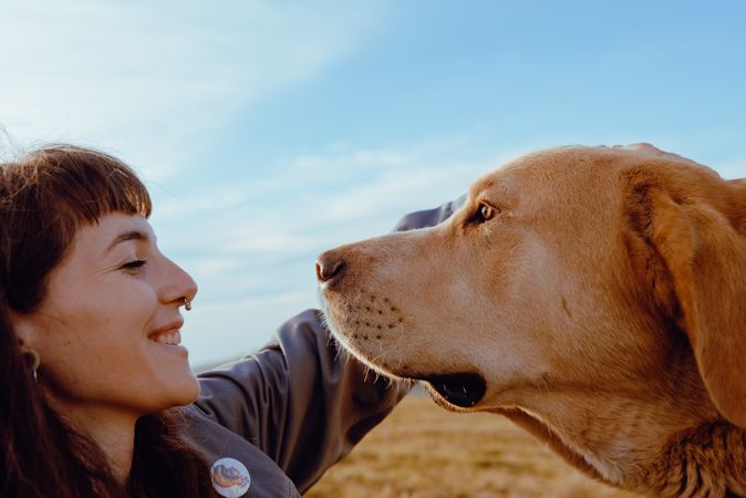 Woman with piercing sitting near dog between field