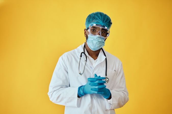 Portrait of medical male doctor in yellow studio with full ppe gear with hands crossed