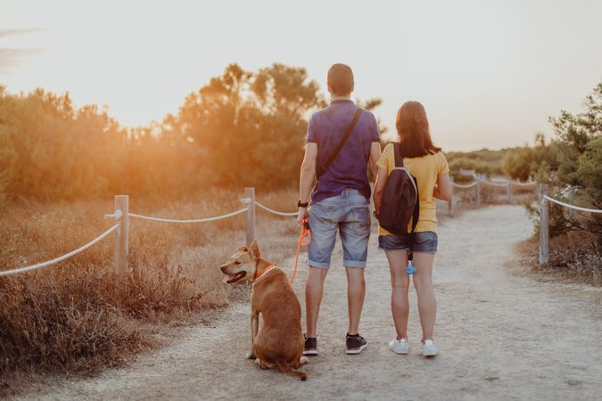Casual adult couple walking with dog along rural pathway