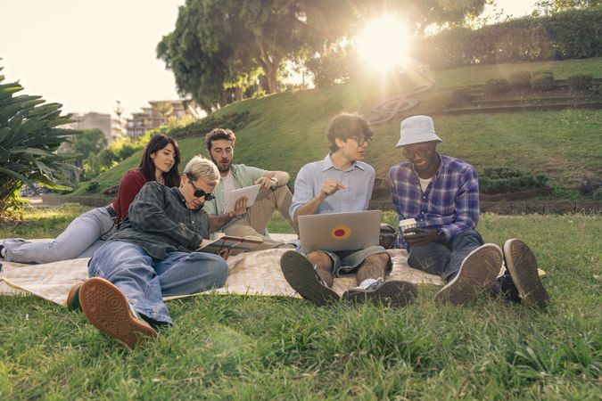 Diverse group of students studying and working together on laptops outdoors.