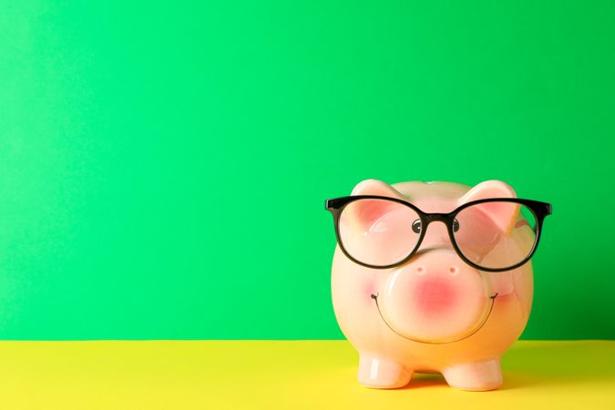 Happy piggy bank with glasses on color table against green background, space for text. Finance, saving money