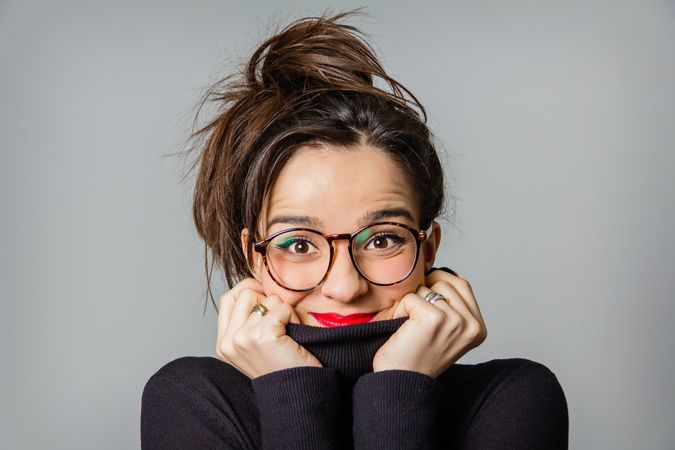 Woman with glasses and red lips taking her neck sweater