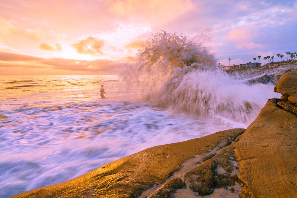 Person standing beside sea wave splashing on rocks
