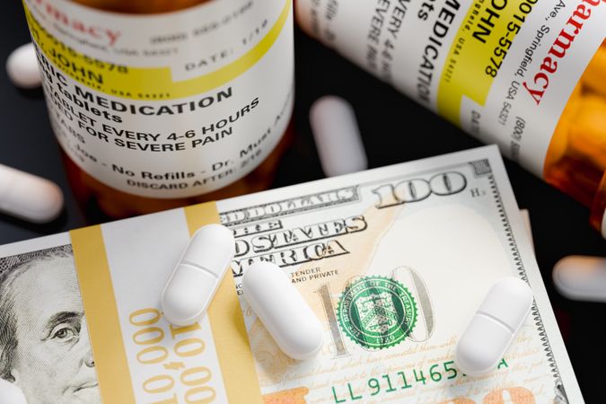 Prescription Medicine Bottles and Pills Next To Stacks of 100 Dollar Bills.