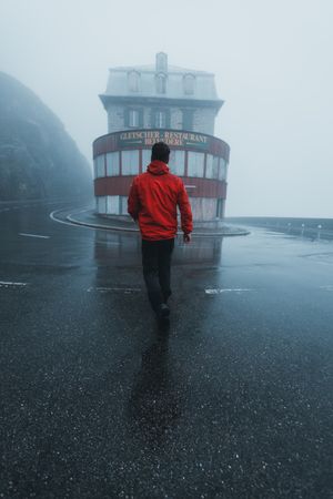 Back view of person in red jacket standing near building under the rain