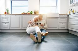Older couple holding each other on the kitchen floor drinking red wine
