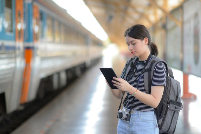 A teen traveler with a tablet and rucksack waiting for a train