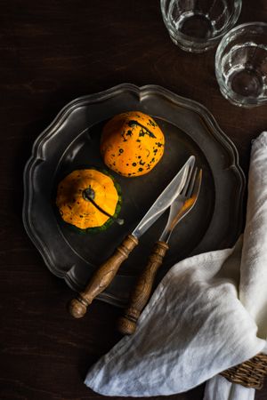 Top view of dark table setting with two squashes and cutlery
