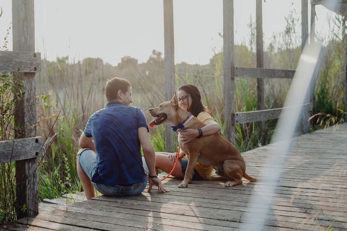 Cheerful adult couple playing with dog at countryside