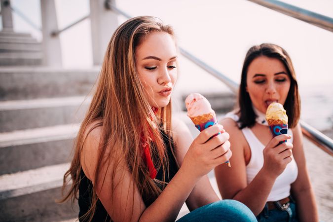 Two young women sitting on the steps outside enjoying ice cream cones