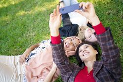 Looking down at three women lying on grass taking photo with smartphone