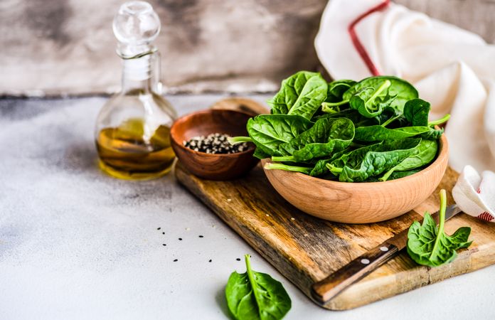 Wooden bowl of fresh spinach leaves on kitchen counter with copy space