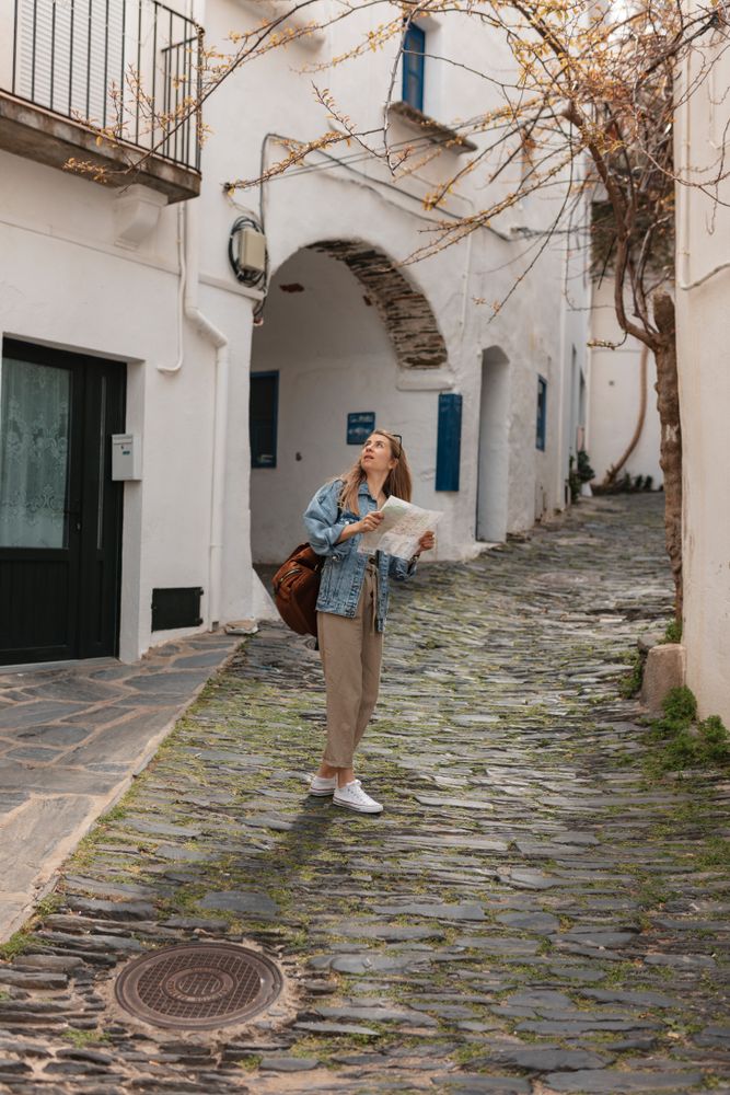 Woman standing in middle of narrow town street holding map and looking up