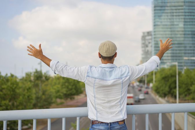Male in denim standing with outstretched arms on bridge over city traffic