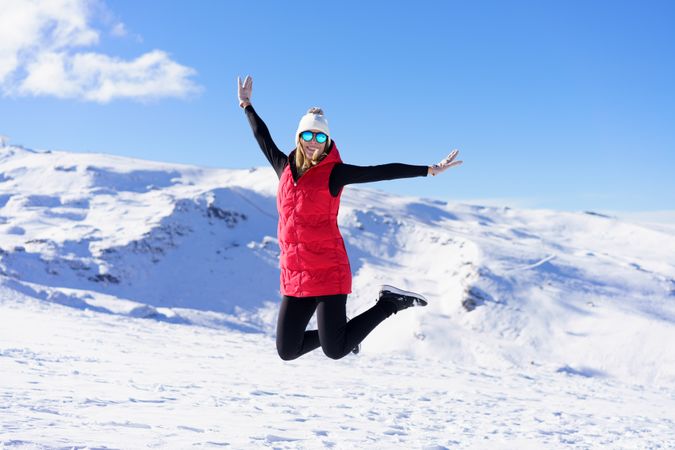Woman in winter gear jumping on snowy mountain