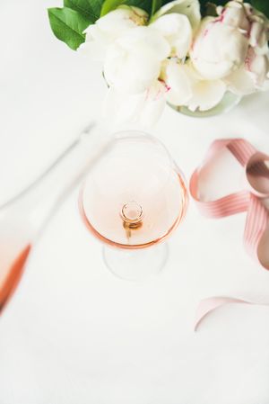 Bottle pouring glass of pink rose wine in the center with flowers and ribbon