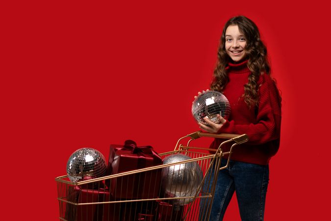 Girl in red sweater holds disco ball near shopping cart