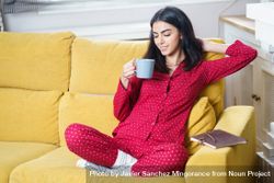 Female sipping tea on yellow sofa at home with notebook at her side 56qGV0