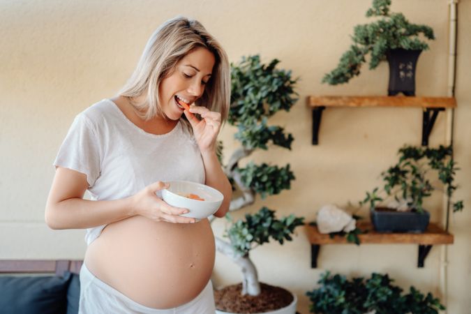 Smiling pregnant woman holding belly at home